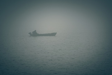lonely fisherman on a boat, heavy fog on the lake
