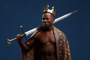 African man in a crown and cloak holds a sword in his hand.