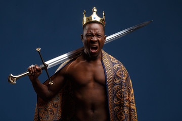 African man in a crown and cloak holds a sword in his hand.