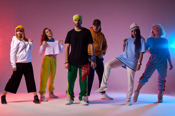 Group of young professional break dancers standing on light coloured background, looking at camera with self assurance, satisfied by good dance performance, full of energy dancers after concert