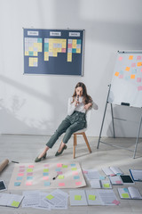 pensive businesswoman sitting on chair near sticky notes on floor