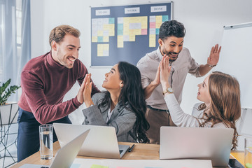 happy multicultural businesswomen and businessmen giving high five in office