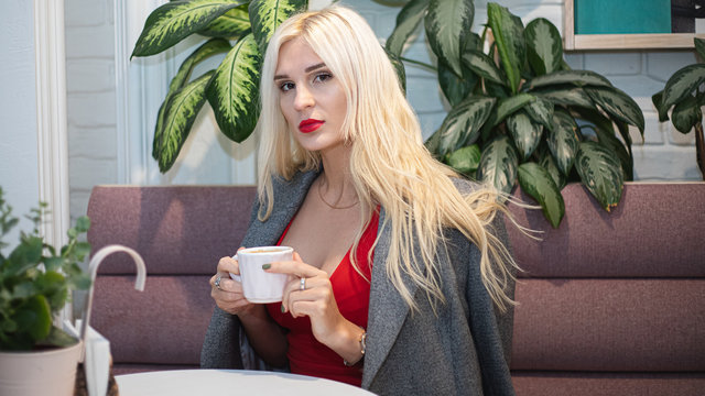 Young beautiful blond woman in an autumn coat seets in the cafe. Soft focus. Fashionable concept.