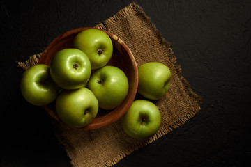 Green apples Simirenko in wooden bowl at black background. 