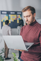 selective focus of handsome businessman using laptop in office
