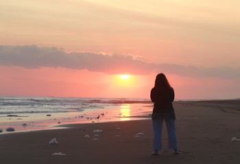 mujer mirando el sol al atardecer en la orilla de la playa