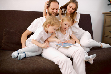 attractive caucasian family in casual clothes sit on sofa wearing casual clothes, looking at screen of tablet. happy family at home