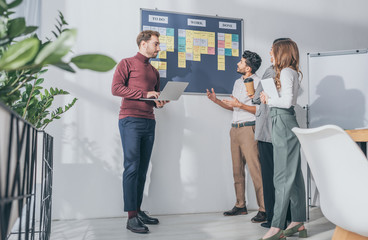 scrum master using laptop near board with letters and multicultural coworkers