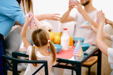caucasian family consisted of mother, father, cute children and their family member friendly white dog celebrating birtday together at home, in kitchen, wearing birthday caps