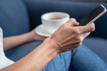 Hands holding a cellphone and tea cup
