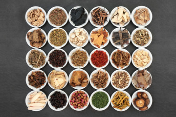 Traditional Chinese herb collection used in herbal medicine in white porcelain bowls on slate...
