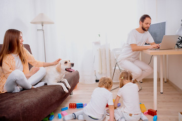 adorable family consisted of mother, father and kid girl at home in living room, in casual white...