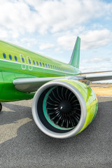 Vertical photo of green modern civil passenger aircraft on airfield. On the foreground a close-up...