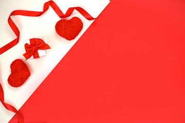 The concept of the holiday Valentine's Day. Two hearts of red cotton yarn, a gift in white wrapping paper on a double white-red background.