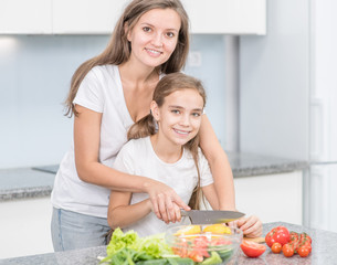 Happy family at home. Mom teaches her daughter to cut vegetables for vegetable salad