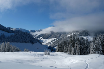 Fototapeta na wymiar Beautiful panorama of snow covered Kitzbuehleler Horn, Austrian alps mountain peak. Low clouds hang around the mountain ranges and over the valley. Glittering shiny deep fresh powder snow foreground.