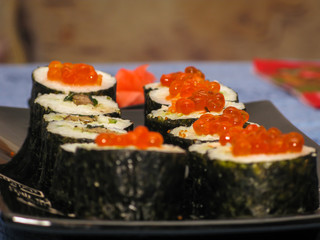 sushi decorated with red caviar on a black traditional plate