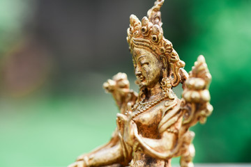 Fototapeta na wymiar Figure of a female Buddhist deity (Green Tara) sitting on a lawn 