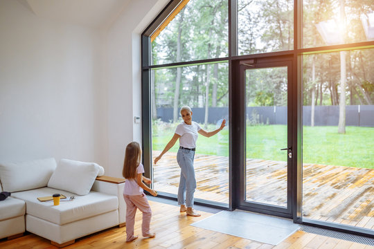 Mother And Daughter Near Panoramic Window Together, Relaxing Together, Spending Time At Home. Modern House Interior