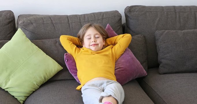 six years old child lying comfortably on a brown sofa resting her head on her hands