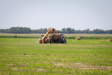 Tractor loading hay bales on truck agricultural works