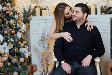 Christmas and New Year concept.  The bearded man sits and his wife hugs him from behind. Family in the studio. Pregnant family, mom and dad in family look. Pregnant couple in love.