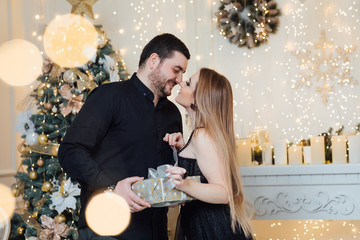 Family standing in the studio. Attractive girl and man with beard near Christmas tree. Pregnant woman with her husband. A beautiful young loving couple with Christmas gifts. Woman unleashes a gift bow