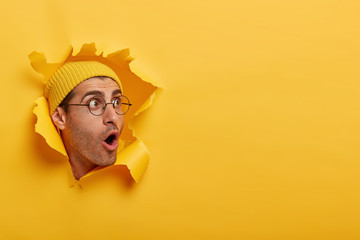 Stunned man looks with great surprisement or fear aside, opens mouth widely, wears hat and round...