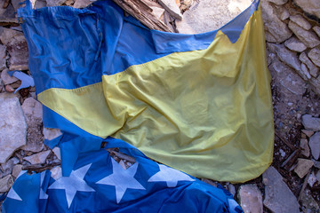 Torn flag of Bosnia and Herzegovina on the ground. Lost in the rubble. Representation of division of serbian,croatian and muslim nations. War in Bosnia