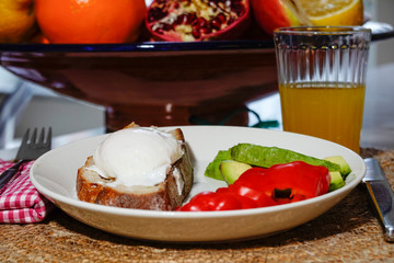 A poched egg with bread, avocado and peppers on a plate, with a ginger shot.