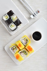 Japanese rolls on plates with soy sauce, chopsticks, beautiful. Vertical, light background. Top view.