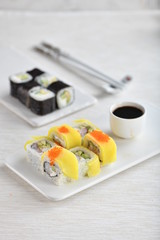 Japanese rolls on plates with soy sauce, chopsticks, beautiful. Vertical, light background.
