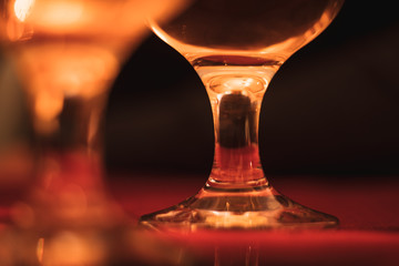 Closeup of the bottom of a wine glass with another blurred in foreground. Dark black background,...