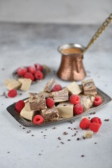 Oriental sweets, halva slices on a metal dish, decorated with raspberries, with Turkish coffee. Background, vertical.