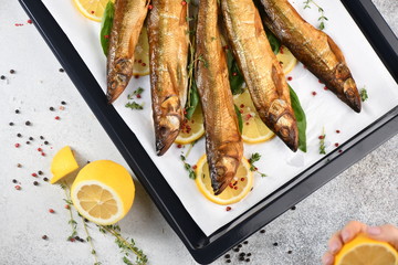 Whole fish, fried or smoked, on a baking sheet with lemon and herbs. Top view.