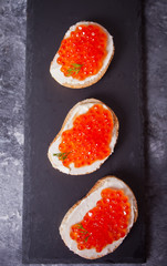 Fresh red caviar on bread on the black plate. Sandwiches with red caviar. Delicatessen. Gourmet food.
