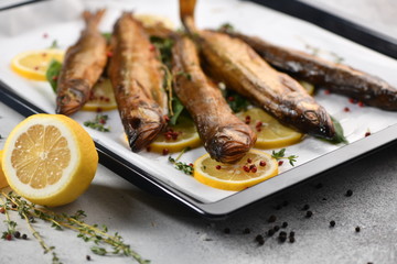Whole fish, fried or smoked, on a baking sheet with lemon and herbs.