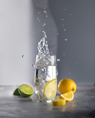 Glass with water, ice. Near lemon, citrus, lime. Throw ice, fly spray, wave.