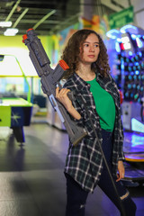 Obraz na płótnie Canvas Beautiful girl with curly hair and plaid shirt with a toy gun from a shooting simulator