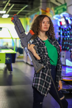 Beautiful girl with curly hair and plaid shirt with a toy gun from a shooting simulator
