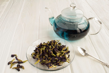 Blue flower tea in the glass  saucer and glass  teapot  the white wooden background. Closeup. Copy space.
