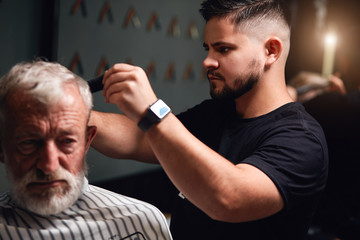 attrcative bearded stylist brushing senior man's hair, close up photo