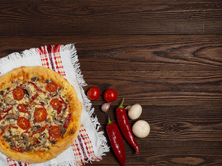 Homemade pizza with minced meat, red pepper, mushrooms and tomatoes lies on a natural wooden...