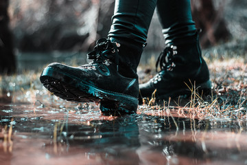 Closeup of two woman's black boots, walking on a puddle in the field. Cold rainy winter day, bad...