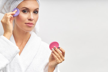 Young woman in bathrobe and towel use beauty sponges. Isolated over white background