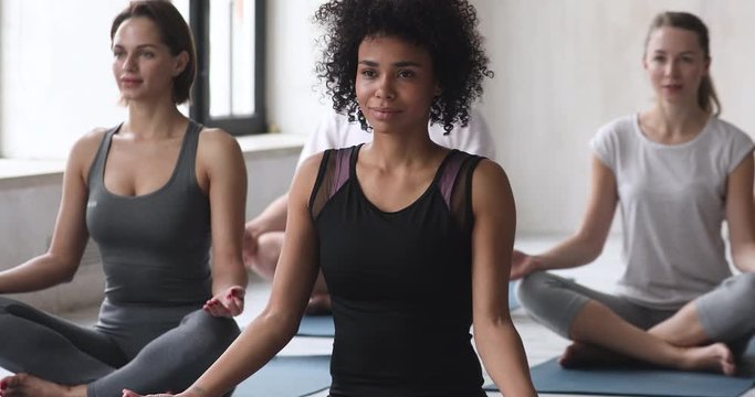 Sporty people group seated in lotus pose meditating together indoors