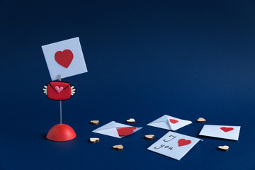 Fototapeta na wymiar Valentine's day. On a paper background of blue color is the holder to which the Valentine is attached. There are other envelopes with messages and wooden, small hearts. Closeup composition.