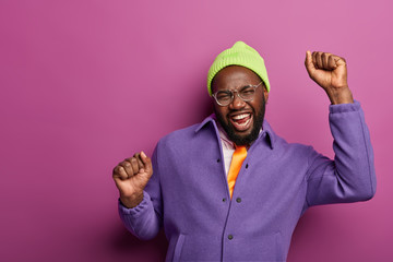 Glad enthusiastic bearded man keeps hands up, celebrates triumph, makes champion dance, celebrates...