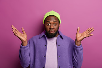 Who cares? Hesitant black bearded man spreads palms with questioned look, doesnt see way out in...