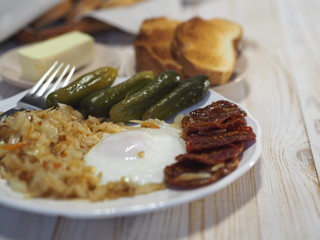 Home cooking. Fried cabbage, egg, pickles and dried tomatoes on a white plate on a wooden table. Bachelor breakfast.